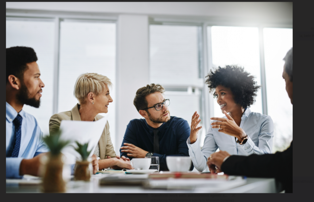 Ein diverses Team diskutiert in einem modernen Büro. Eine Frau mit lockigen Haaren erklärt gestikulierend etwas, während die anderen aufmerksam zuhören.